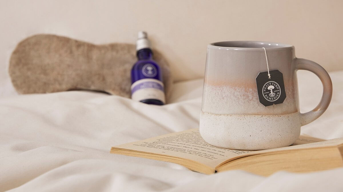 A mug of tea and Goodnight Pillow Mist sit on a bed