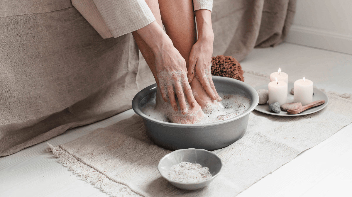 A woman bathes her hands and feet in a foot bath with candles and salts next to it