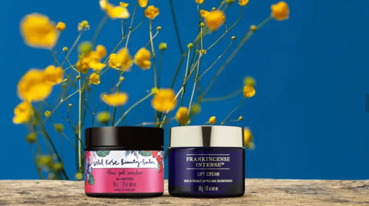 Wild Rose Beauty Balm and Frankincense Intense Lift cream with flowers behind them