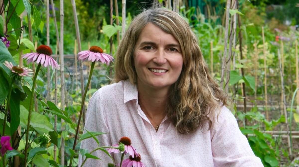 Tipper its in her garden with pink flowers in front of her, smiling at the camera